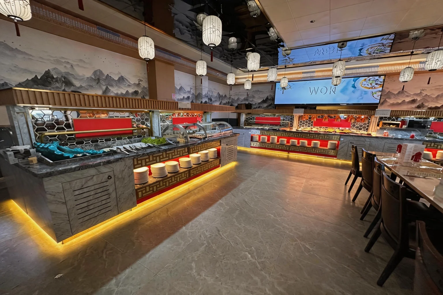 Buffet counters with a lit screen reading WOK, beneath an ink-wash mountain mural