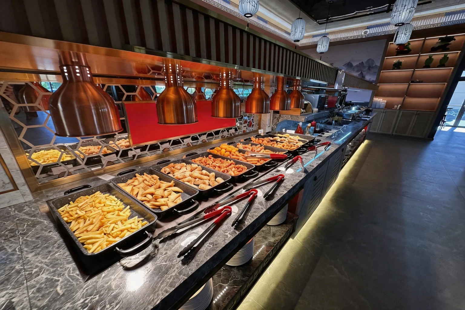 Trays of fries, samosas and chicken nem spring rolls on the buffet counter, under copper pendant lights